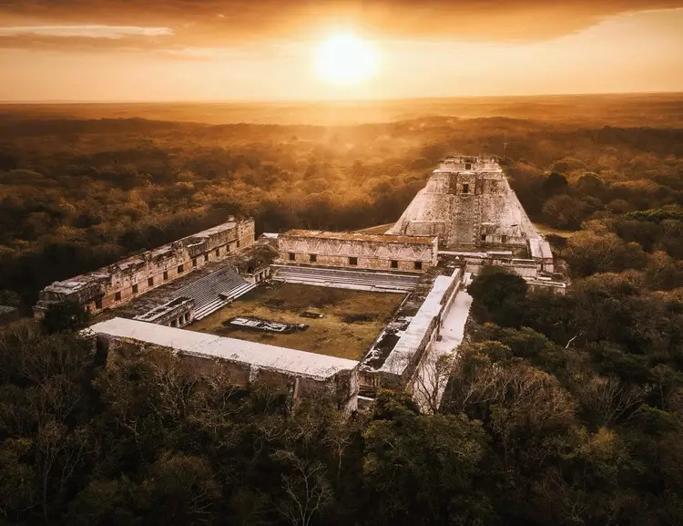 Ancient stone pyramid and palace structures sit surrounded by dense forest under a golden sunset sky
