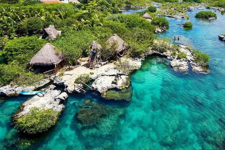 Thatched-roof structures and wooden docks sit on rocky outcrops surrounded by turquoise water and dense green vegetation