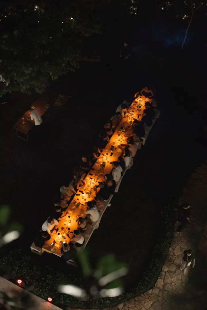 Aerial view of an illuminated wooden boardwalk at night surrounded by trees, with people walking along the lit pathway Aerial view of an illuminated wooden boardwalk at night surrounded by trees, with people walking along the lit pathway