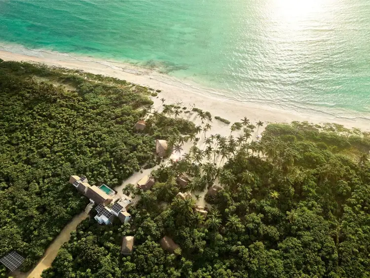 Aerial view of a beachfront property nestled between dense tropical forest and turquoise ocean water with white sand beach Aerial view of a beachfront property nestled between dense tropical forest and turquoise ocean water with white sand beach
