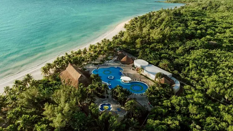 Resort with blue pools nestled among palm trees and tropical vegetation along a turquoise beach Resort with blue pools nestled among palm trees and tropical vegetation along a turquoise beach