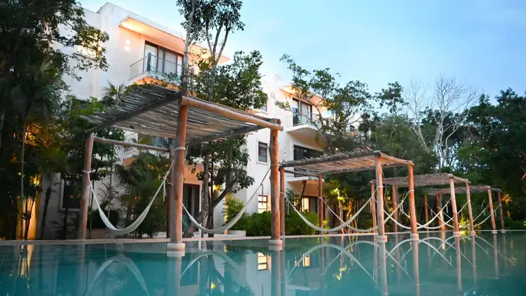 Modern resort with white and wood architecture features a swimming pool, wooden pergolas, and tropical vegetation at dusk Modern resort with white and wood architecture features a swimming pool, wooden pergolas, and tropical vegetation at dusk