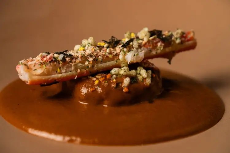 Grilled shrimp skewer topped with seasoned breadcrumbs sits on a brown sauce on a plate Grilled shrimp skewer topped with seasoned breadcrumbs sits on a brown sauce on a plate