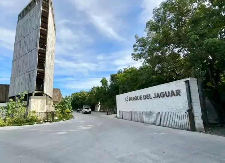 An abandoned concrete tower stands beside a street entrance marked with a sign, with trees and overgrown vegetation surrounding the area