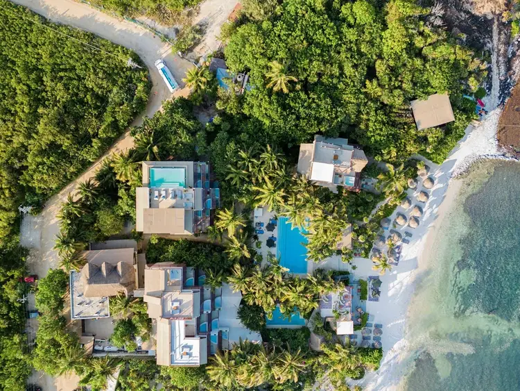 Aerial view of a beachfront resort nestled among tropical vegetation with pools, buildings, and sandy beach visible along the coastline