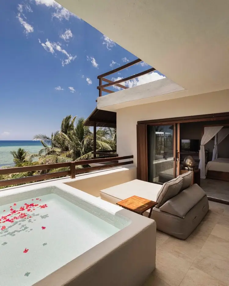 Oceanfront resort terrace with an infinity pool decorated with flower petals, lounge seating, and views of palm trees and turquoise water below