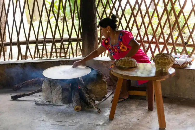 Woman in pink shirt works at a traditional cooking surface in an open-sided structure with woven walls Woman in pink shirt works at a traditional cooking surface in an open-sided structure with woven walls