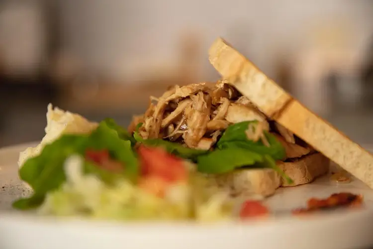 Sandwich with shredded meat, lettuce, and tomato on toasted bread served on a white plate Sandwich with shredded meat, lettuce, and tomato on toasted bread served on a white plate