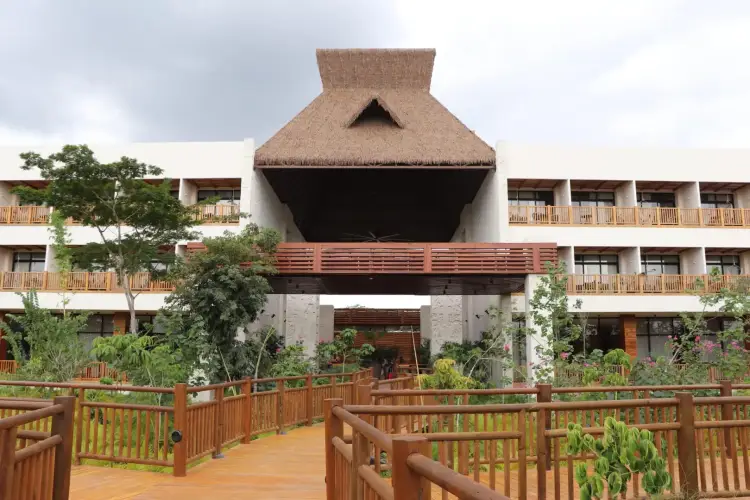 Modern multi-story resort building with thatched roof entrance, wooden railings, and manicured landscaping Modern multi-story resort building with thatched roof entrance, wooden railings, and manicured landscaping