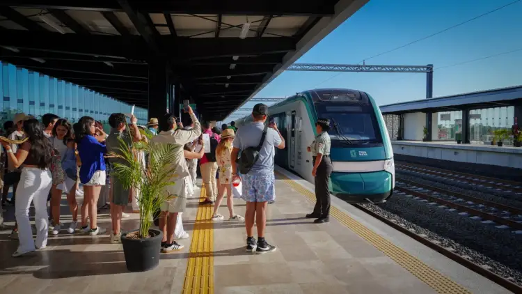 Passengers board a teal and white train at a modern platform station under a covered structure on a clear day Passengers board a teal and white train at a modern platform station under a covered structure on a clear day