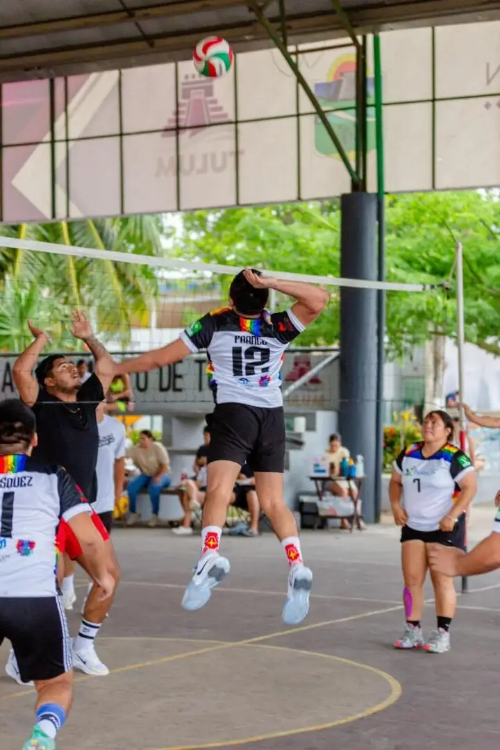 A volleyball player jumps to spike the ball during a competitive match on an outdoor court under a covered structure, with teammates and opponents nearby A volleyball player jumps to spike the ball during a competitive match on an outdoor court under a covered structure, with teammates and opponents nearby
