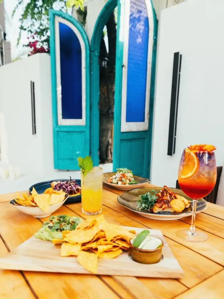 Wooden outdoor table set with tacos, chips, salads and cocktails in front of turquoise doors and white walls Wooden outdoor table set with tacos, chips, salads and cocktails in front of turquoise doors and white walls