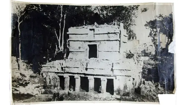 Weathered stone structure with multiple levels and dark openings set among trees in a forested area Weathered stone structure with multiple levels and dark openings set among trees in a forested area