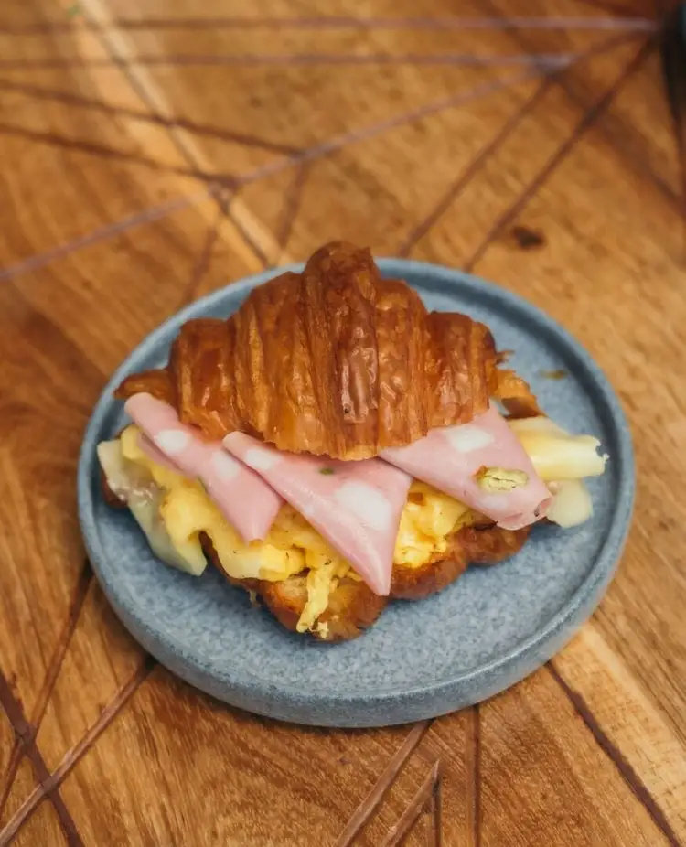 Croissant sandwich with scrambled eggs and ham slices on a gray plate on a wooden table Croissant sandwich with scrambled eggs and ham slices on a gray plate on a wooden table