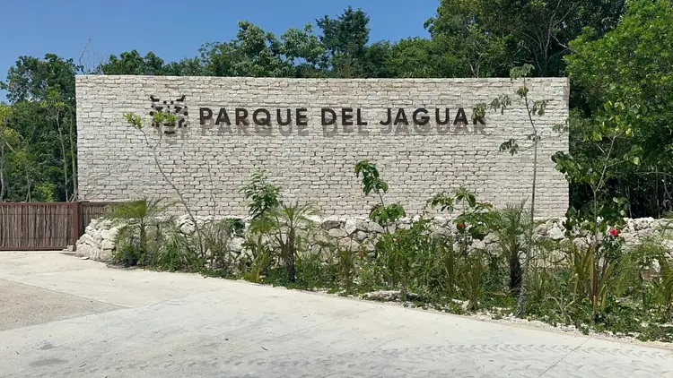 White brick entrance wall with "Parque del Jaguar" text, surrounded by tropical vegetation and trees under clear sky