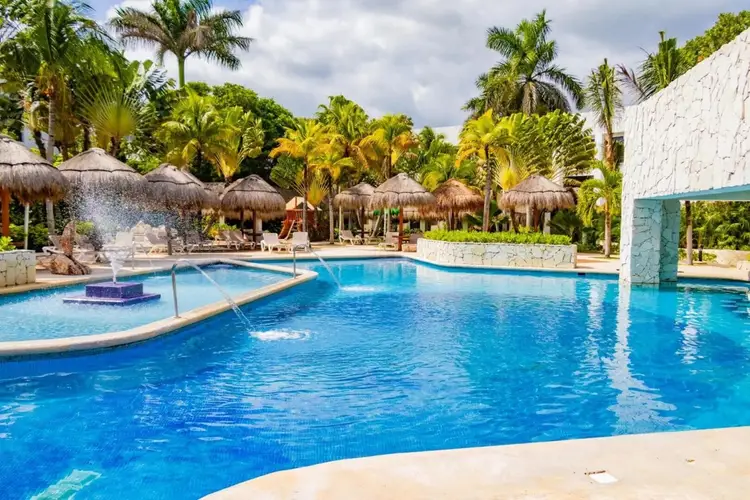 Resort swimming pool with thatched umbrellas, lounge chairs, and palm trees surrounding the blue water Resort swimming pool with thatched umbrellas, lounge chairs, and palm trees surrounding the blue water