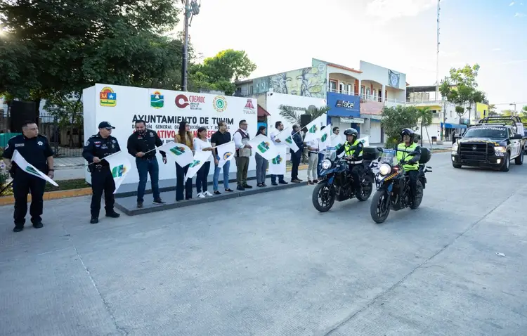 Police officers and officials stand along a street banner during a safety initiative event, with motorcycle officers and patrol vehicles present Police officers and officials stand along a street banner during a safety initiative event, with motorcycle officers and patrol vehicles present