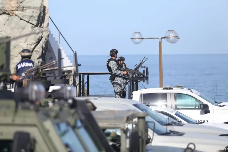 Armed National Guard personnel stand guard at a waterfront location with vehicles and ocean visible in the background Armed National Guard personnel stand guard at a waterfront location with vehicles and ocean visible in the background