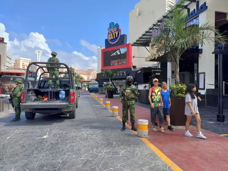 Military personnel in uniform stand guard on a downtown street lined with shops and entertainment venues while pedestrians walk nearby Military personnel in uniform stand guard on a downtown street lined with shops and entertainment venues while pedestrians walk nearby