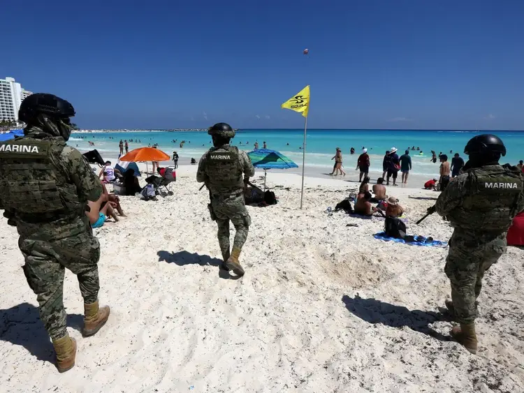 Military personnel in camouflage uniforms patrol a crowded beach with turquoise water and white sand under clear blue sky Military personnel in camouflage uniforms patrol a crowded beach with turquoise water and white sand under clear blue sky