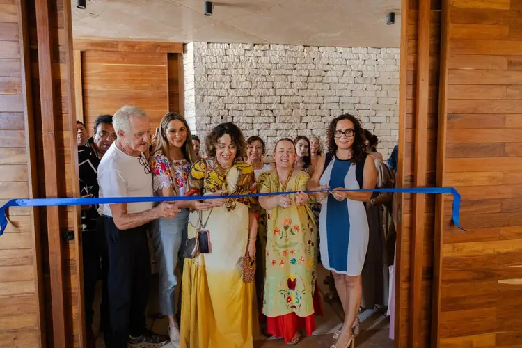 A group of people hold a blue ribbon across a doorway during what appears to be a ribbon-cutting ceremony inside a building with wooden and brick walls A group of people hold a blue ribbon across a doorway during what appears to be a ribbon-cutting ceremony inside a building with wooden and brick walls