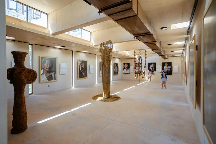 Gallery interior with sculptures and framed portraits on walls, visitors walking through a bright, open exhibition space with skylights Gallery interior with sculptures and framed portraits on walls, visitors walking through a bright, open exhibition space with skylights