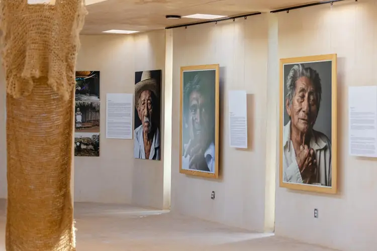Gallery space with framed portrait photographs and informational panels hung on white walls beside a brick column Gallery space with framed portrait photographs and informational panels hung on white walls beside a brick column