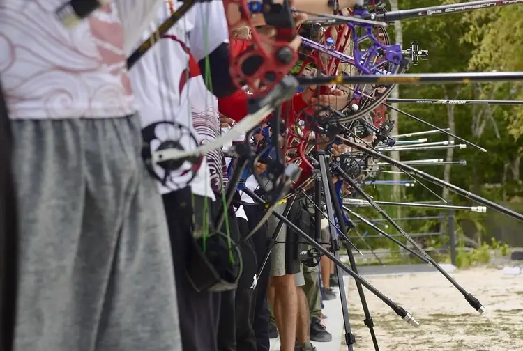 Young archers stand with their bikes near a wooden fence at an outdoor practice area surrounded by trees Young archers stand with their bikes near a wooden fence at an outdoor practice area surrounded by trees
