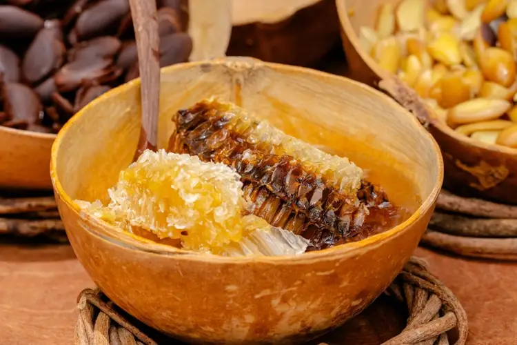 Honeycomb pieces in a wooden bowl with a wooden spoon, surrounded by cacao beans and nuts on a rustic surface Honeycomb pieces in a wooden bowl with a wooden spoon, surrounded by cacao beans and nuts on a rustic surface