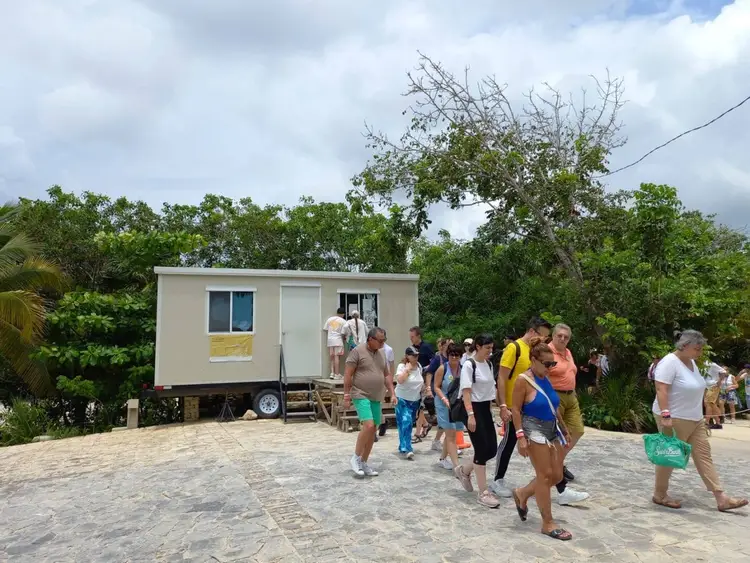 A group of visitors walks around a mobile trailer structure positioned on a concrete platform surrounded by tropical vegetation