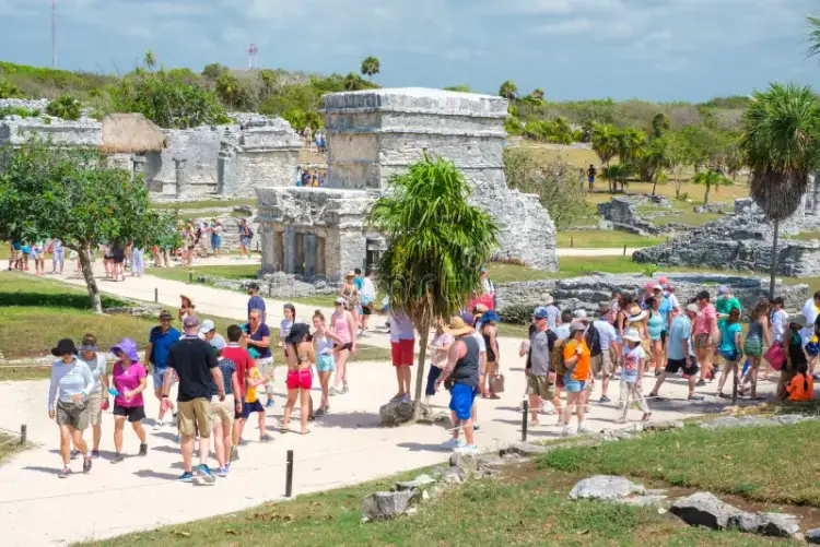 Tourists walk among ancient stone ruins and structures in a tropical archaeological site surrounded by vegetation Tourists walk among ancient stone ruins and structures in a tropical archaeological site surrounded by vegetation