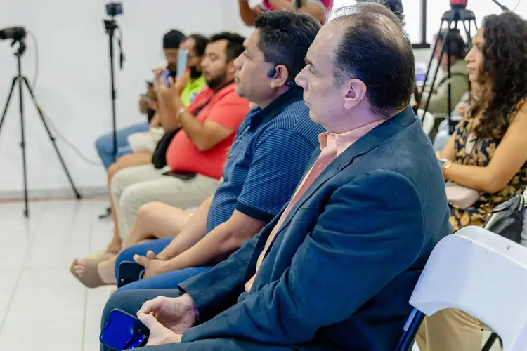 People sit in a row facing away from the camera in an indoor venue with professional lighting and camera equipment visible in the background People sit in a row facing away from the camera in an indoor venue with professional lighting and camera equipment visible in the background