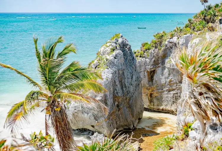 Rocky limestone formations and tropical vegetation overlook turquoise water and a sandy beach at a coastal archaeological site Rocky limestone formations and tropical vegetation overlook turquoise water and a sandy beach at a coastal archaeological site