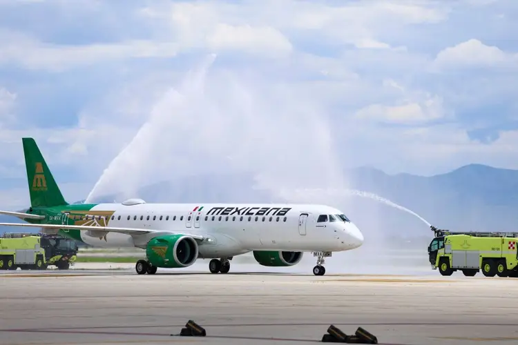 Commercial aircraft receives water cannon salute on tarmac with ground vehicles and mountains in background Commercial aircraft receives water cannon salute on tarmac with ground vehicles and mountains in background