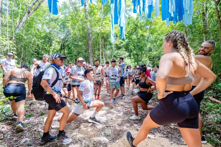Trail runners gather on a wooded path decorated with blue ribbons hanging from trees overhead