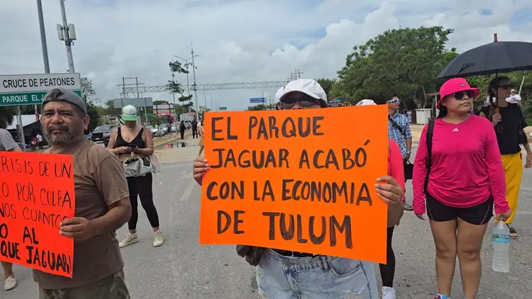Protesters hold orange signs written in Spanish during a street demonstration, with communication towers and buildings visible in the background