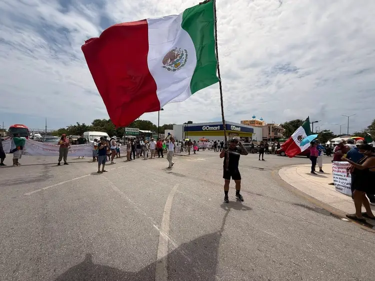 Crowd of people gathered in a parking area holding large Mexican flags during what appears to be a public demonstration or protest