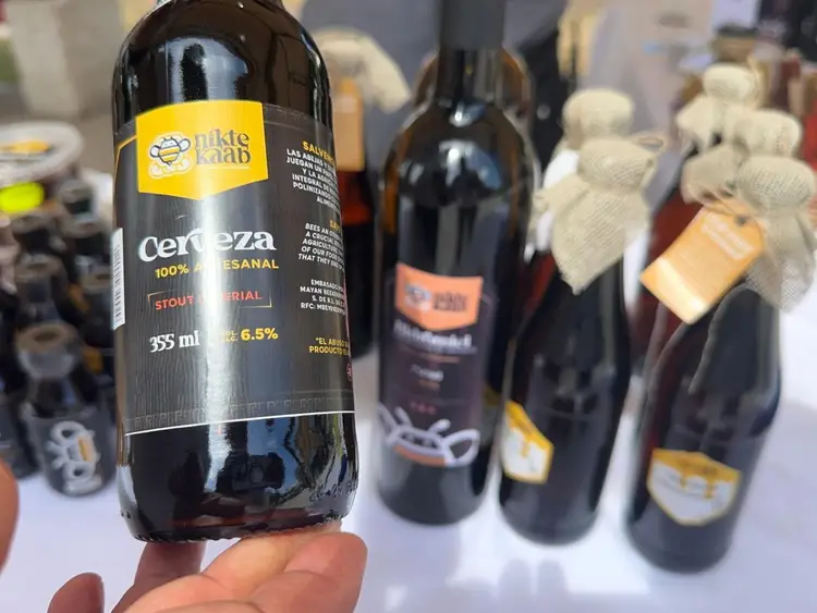 Hand holding a dark beer bottle labeled "cerveza" with a yellow logo, displayed among other craft beer bottles on a table Hand holding a dark beer bottle labeled "cerveza" with a yellow logo, displayed among other craft beer bottles on a table