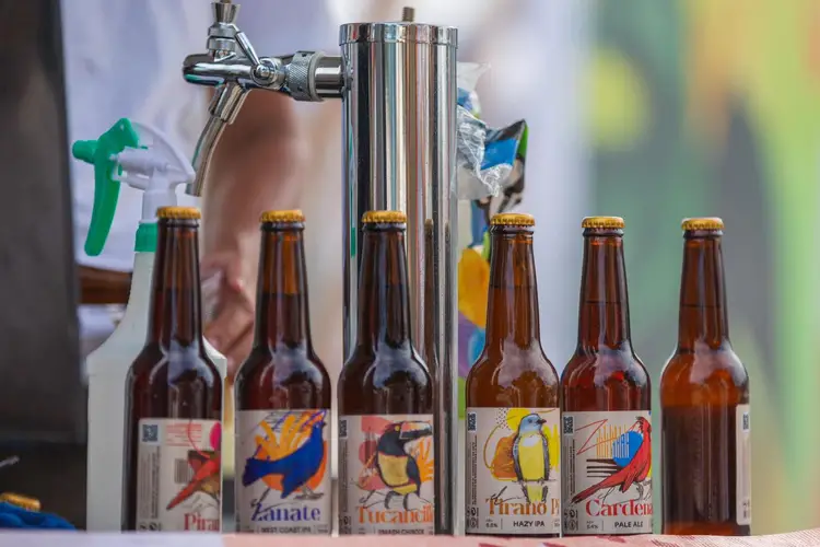 Beer bottles with illustrated labels line up next to a metal tap dispenser at what appears to be a craft brewery display Beer bottles with illustrated labels line up next to a metal tap dispenser at what appears to be a craft brewery display