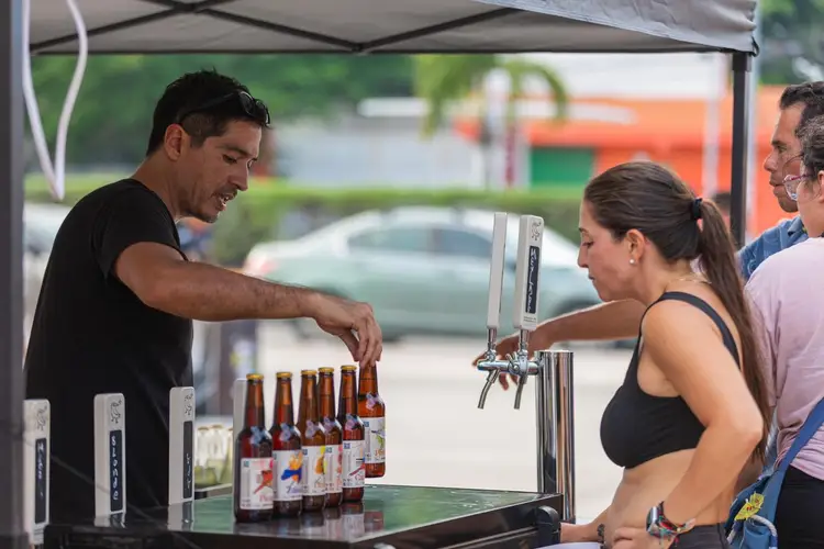 Man serving beer from a tap to a woman at an outdoor vendor stand while another person watches nearby Man serving beer from a tap to a woman at an outdoor vendor stand while another person watches nearby