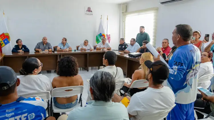 Local residents sit and stand facing officials seated at a table during a community meeting in an indoor government or civic space