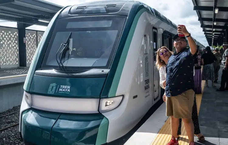 A modern passenger train with green and white livery sits at a station platform while people board and stand nearby A modern passenger train with green and white livery sits at a station platform while people board and stand nearby