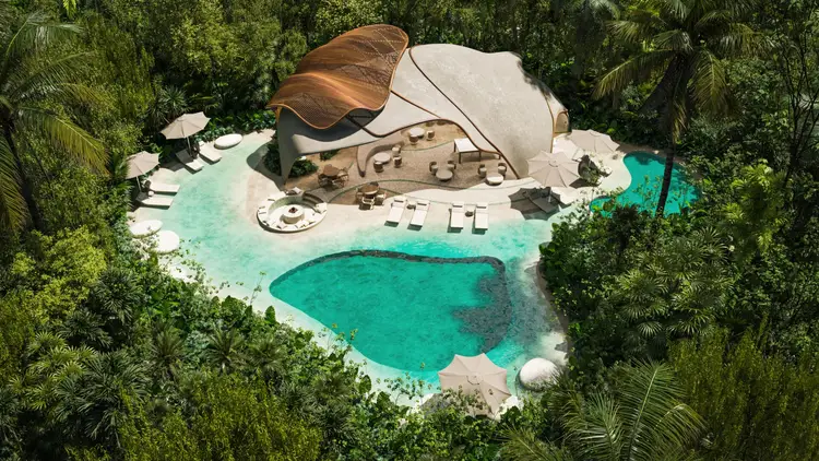 Aerial view of a tropical resort nestled in dense jungle with turquoise lagoons, sandy beach, and large fabric structures surrounded by palm trees