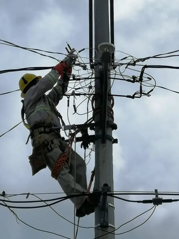 Utility worker in yellow hard hat and safety harness climbs a power pole to work on tangled electrical lines and equipment Utility worker in yellow hard hat and safety harness climbs a power pole to work on tangled electrical lines and equipment