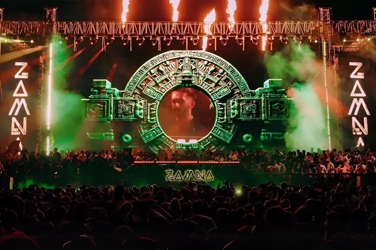 Large outdoor concert stage with ornate circular display and green lighting effects, surrounded by a crowd of attendees at night Large outdoor concert stage with ornate circular display and green lighting effects, surrounded by a crowd of attendees at night
