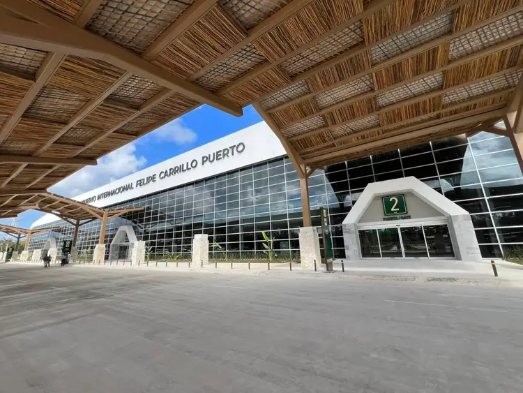 Modern airport terminal with wooden lattice canopy and glass facade sits empty under blue sky
