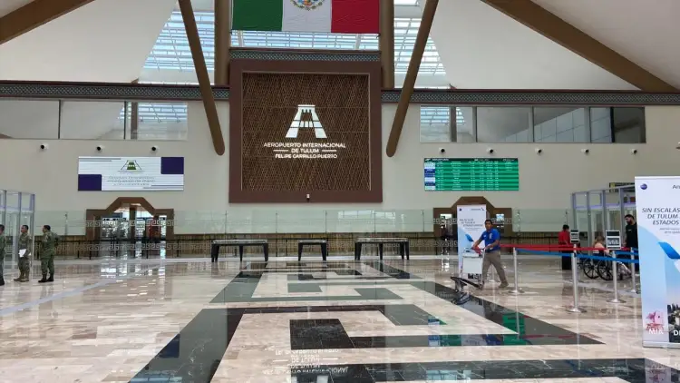 Airport terminal interior with check-in counters, information displays, and a few people walking through the spacious hall beneath wooden ceiling beams