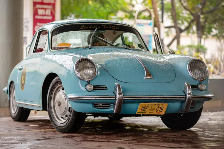 Light blue vintage Porsche with round headlights parked on a street with trees and buildings in the background