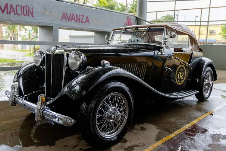 Black convertible classic car with the number 02 on its side parked on wet pavement under a covered structure