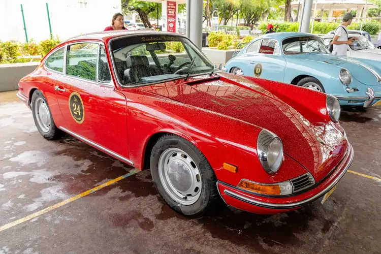Red vintage sports car parked indoors at a classic car exhibition, with another blue vintage car visible behind it